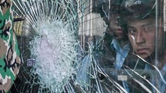 割れたガラス越しに建物の外を眺める警官＝７月１日