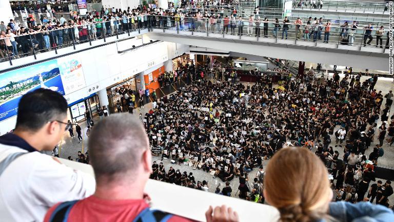 空港での座り込みを眺める旅行客＝７月２６日/Anthony Wallace/AFP/Getty Images