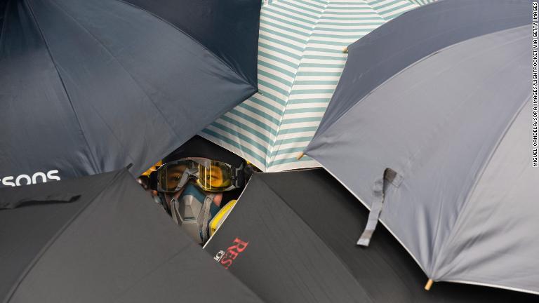 傘のすき間から様子を眺めるデモ参加者＝７月２７日/Miguel Candela/SOPA Images/LightRocket via Getty Images