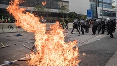 燃え盛る炎を前に後退する警官隊＝２４日、香港・観塘