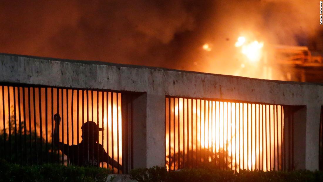 機動隊に石を投げるデモ隊。後ろではゲートが燃えている=24日、ジャカルタ/Achmad Ibrahim/AP