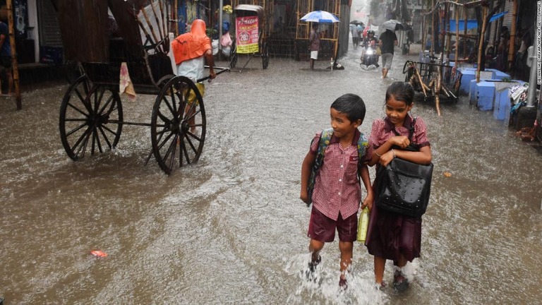 大雨ですねまでつかるほど冠水した道路を歩いて通学するプネーの児童/DIBYANGSHU SARKAR/AFP/AFP/Getty Images