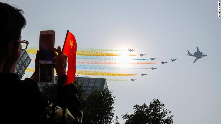 カラフルなスモークをたいて飛ぶ航空機を撮影する人/Andy Wong/AP