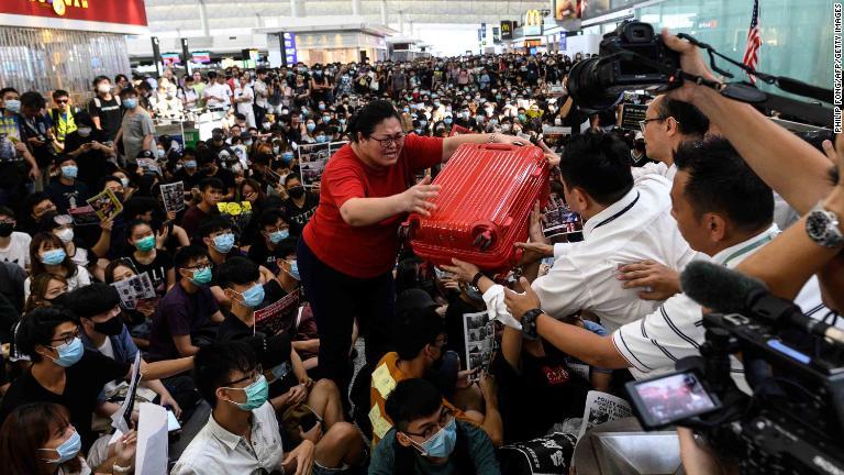 デモ参加者によって混雑する空港ターミナルから出ようする旅行者/Philip Fong/AFP/Getty Images