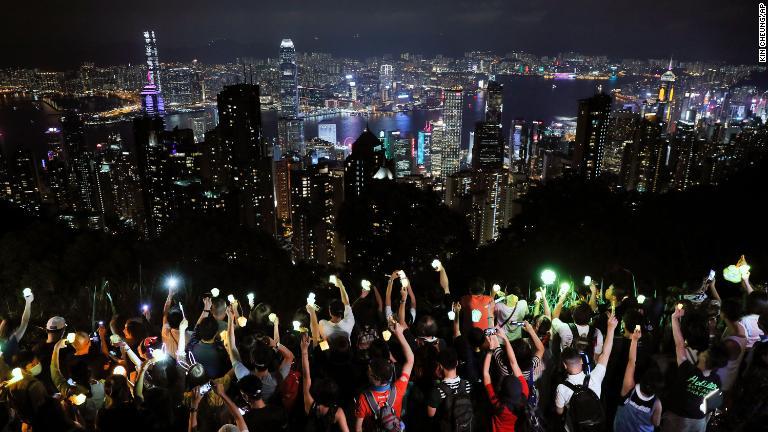 人気の観光スポットで、ライトをつけた携帯電話を掲げるデモ参加者＝９月１３日/Kin Cheung/AP