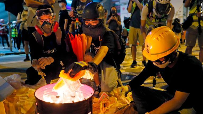 負傷者に敬意を払うために紙のお札を燃やすデモ参加者/Kin Cheung/AP