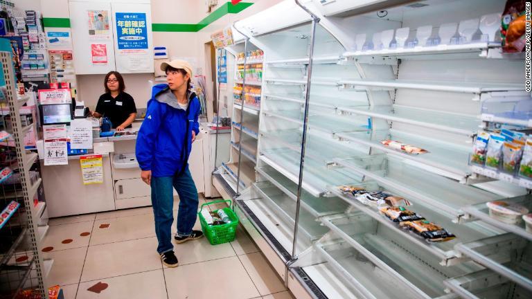 空っぽになった棚を眺める買い物客＝１２日、東京都/Odd Anderson/AFP/Getty Images