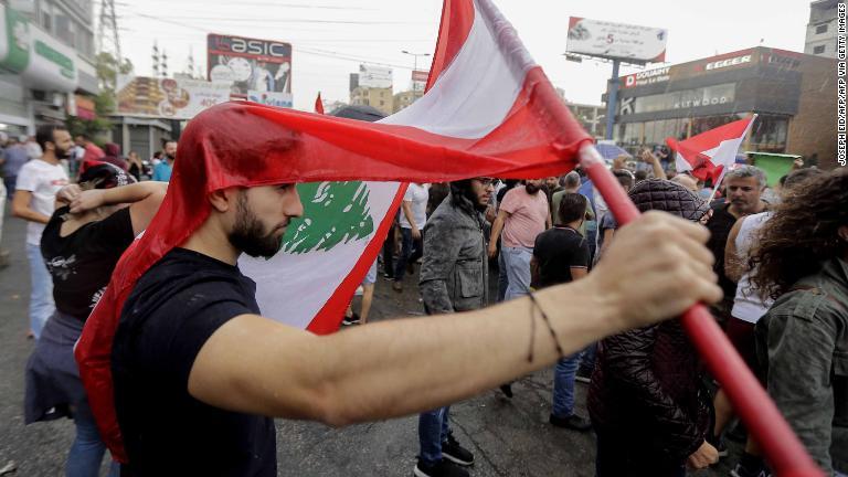 降雨のために顔を国旗で覆う抗議者＝２３日/Joseph Eid/AFP via Getty Images
