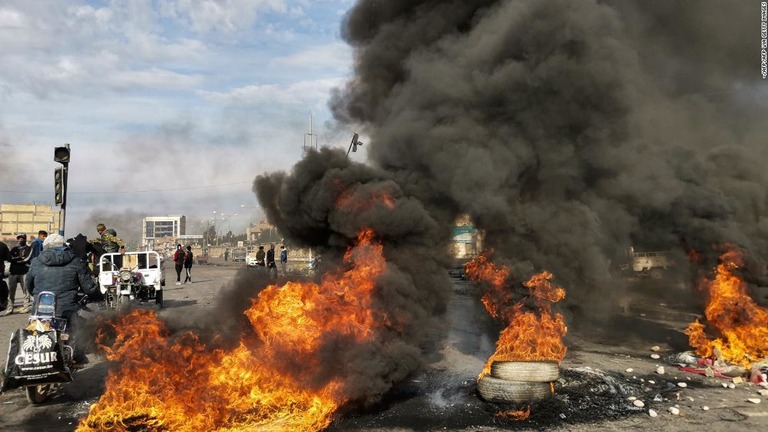 燃えるタイヤの近くに立つ反政府デモの参加者＝２５日、イラク南部ナシリヤ/-/AFP/AFP via Getty Images