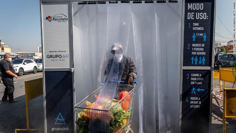 チリの野菜市場で商品とともに消毒装置の中を通過する買い物客/Cristbal Olivares/Bloomberg/Getty Images
