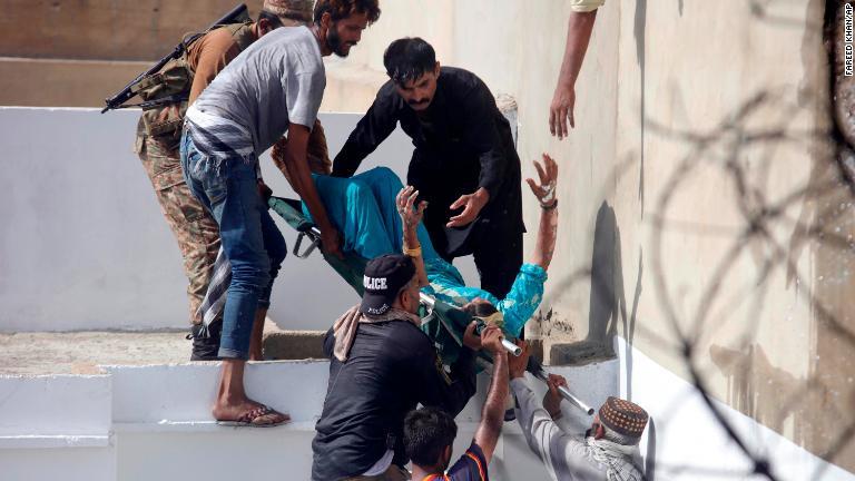 負傷者を運び出す救急要員。機体は国際空港に近い住宅密集地に墜落した/Fareed Khan/AP