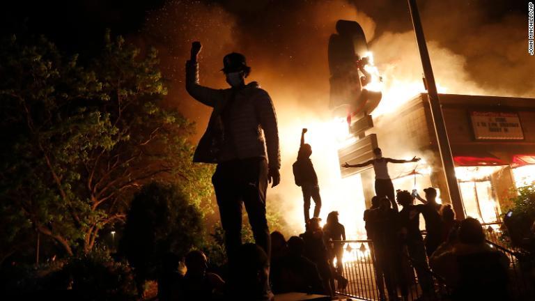 炎上するファストフード店の前に集まるデモ参加者/John Minchillo/AP
