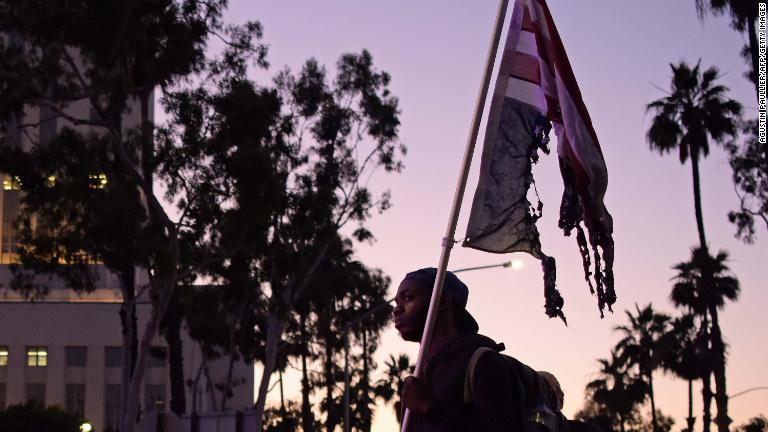 燃やした後の星条旗を掲げるデモ参加者/Agustin Paullier/AFP/Getty Images