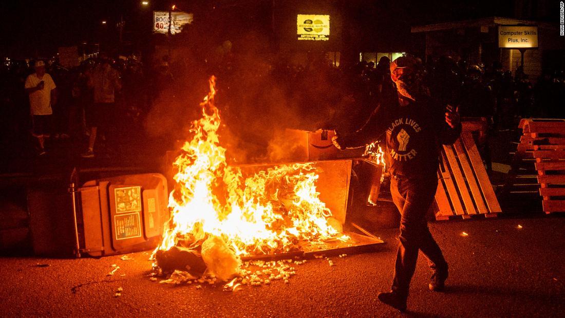 放火されたごみ箱の脇を通り過ぎるデモ参加者＝９月５日、ポートランド/Noah Berger/AP