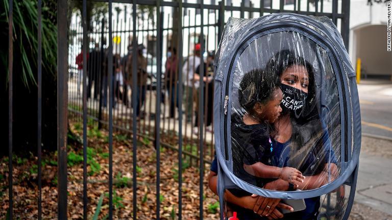 ニューオーリンズで期日前投票の開始日に１８カ月の息子のマンソンくんとともに市庁舎の投票の列に並ぶダナ・クラークさん。マンソンくん用のマスクがなく、どれだけの人がマスクをつけているかわからない状況を考えて、保護用のカバーをまとったという。普段は教壇に立つ＝１０月１６日/Kathleen Flynn/Reuters