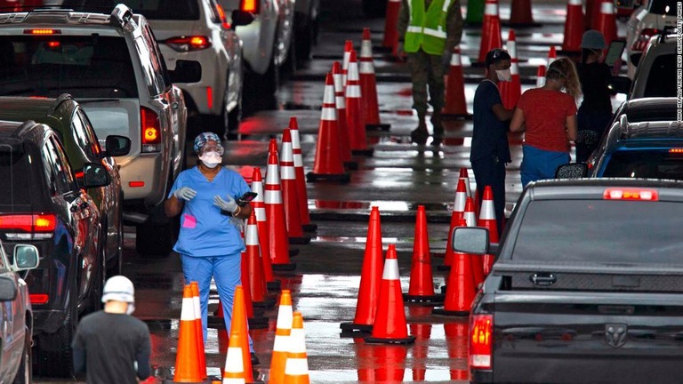 フロリダ州で新型コロナのドライブスルー検査に向かう車列を誘導する医療従事者ら/Miami Herald/Tribune News Service/Getty Images