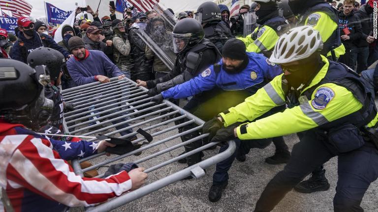 警察のバリケードを突破しようとするトランプ氏支持者/John Minchillo/AP
