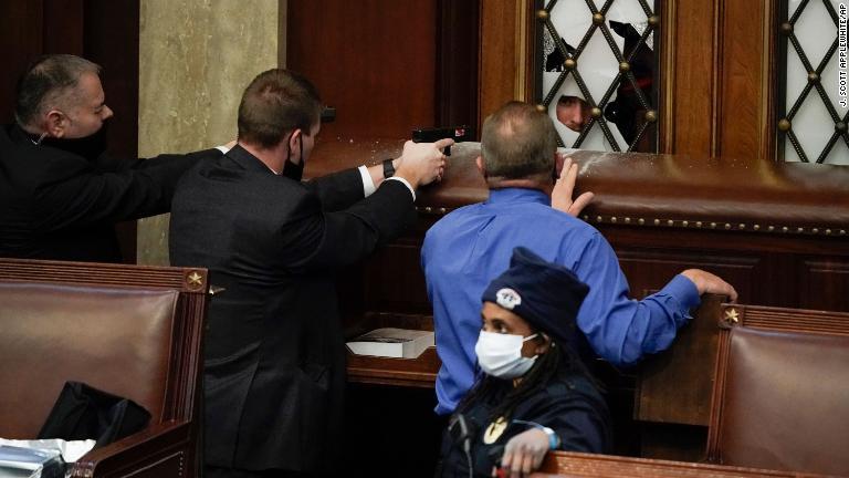 法執行当局者がドアに向けて銃の照準を合わせる。議事堂に暴徒が侵入し下院議場のドアが破壊された/J. Scott Applewhite/AP
