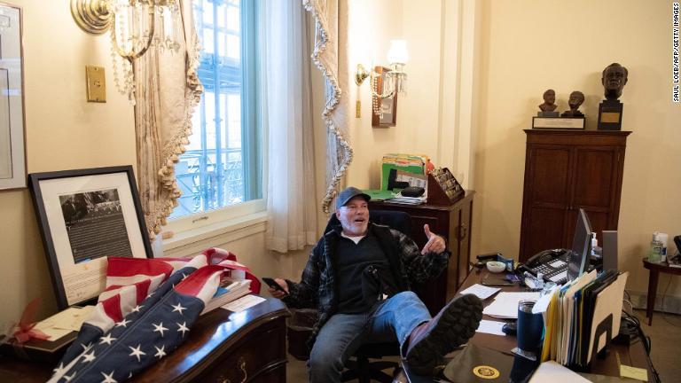 銃推進派の権利擁護団体のリーダー、リチャード・「ビゴ」・バーネット氏がペロシ下院議長のいすに座る様子。その後ペロシ氏のデスクから取ったという封筒を記者団に見せた/Saul Loeb/AFP/Getty Images