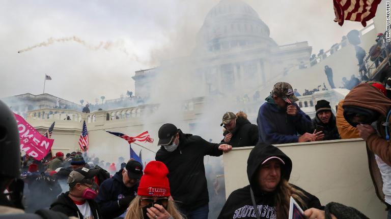 議事堂前に催涙ガスが投げ込まれ顔を覆うトランプ氏支持者/Leah Millis/Reuters