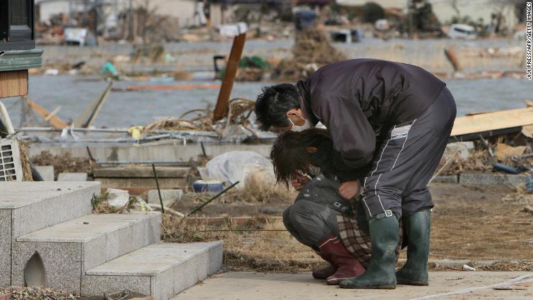 男性が損壊した自宅の前で泣き崩れる女性を慰める。宮城県亘理町/JIJI PRESS/AFP/Getty Images