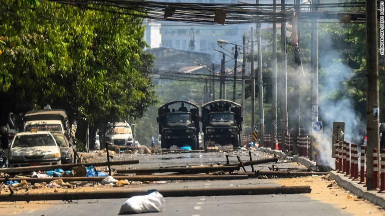 軍用トラックがくすぶるバリケードの近くに並ぶ。バリケードはデモ隊が築き、兵士が火をつけた＝１０日、ヤンゴン/Stringer/AFP/Getty Images