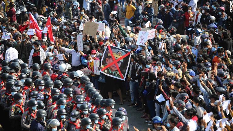 指を３本立てた腕を上げて警察と対峙するデモ隊＝２月８日、ヤンゴン/AP Photo