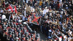 指を３本立てた腕を上げて警察と対峙するデモ隊＝２月８日、ヤンゴン