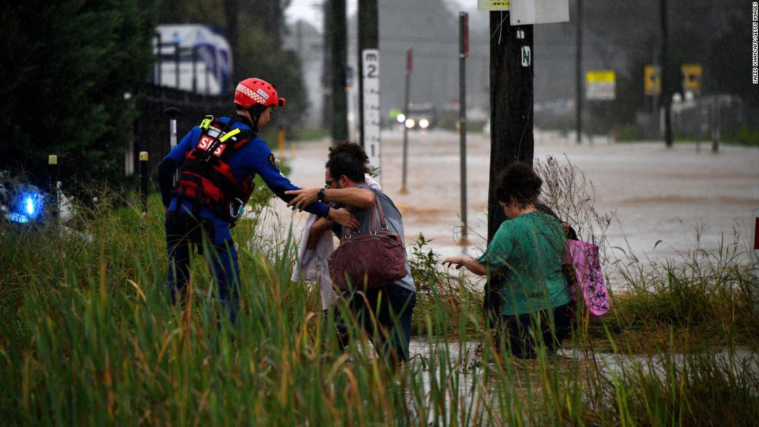 冠水した道路を移動する住民を助ける救急隊員=20日、オーストラリア・シドニー西部/Saeed Khan/AFP/Getty Images