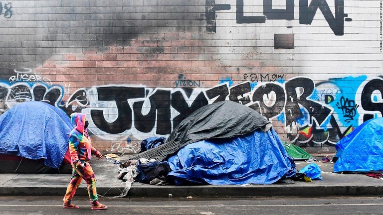 ロサンゼルスの街路に並ぶホームレスのテントの横を歩く女性/Frederic J. Brown/AFP/Getty Images
