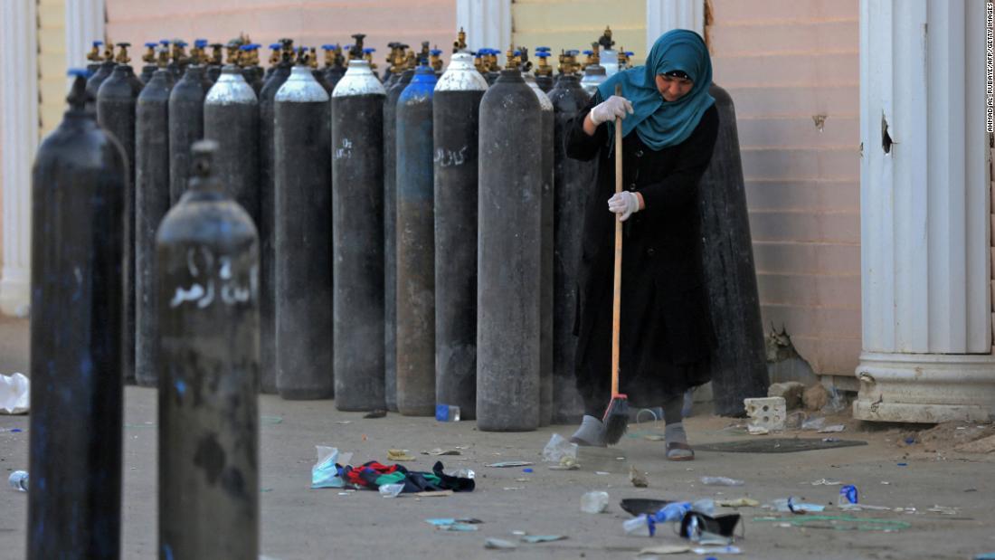 病院の外に運び出された酸素タンクの周囲を清掃する女性＝２５日/Ahmad Al-Rubaye/AFP/Getty Images