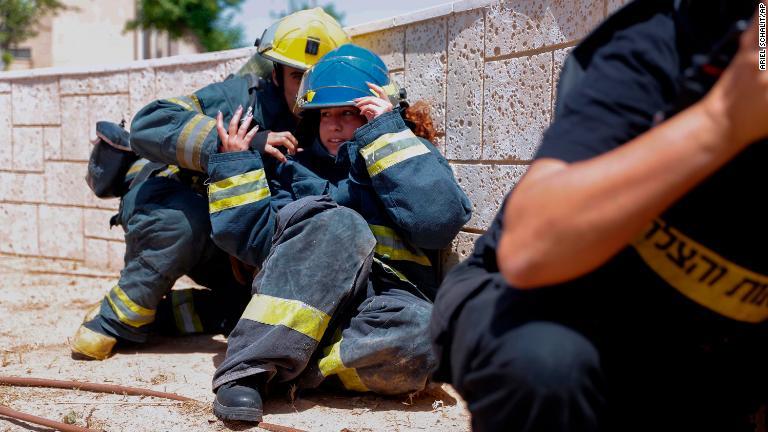 サイレンが鳴り物陰に隠れるイスラエルの消防士＝１１日/Ariel Schalit/AP