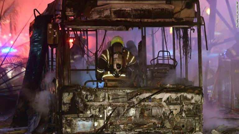 燃えるバスの消火を行う消防士＝１１日、イスラエル・ホロン/Avshalom Sassoni/AP