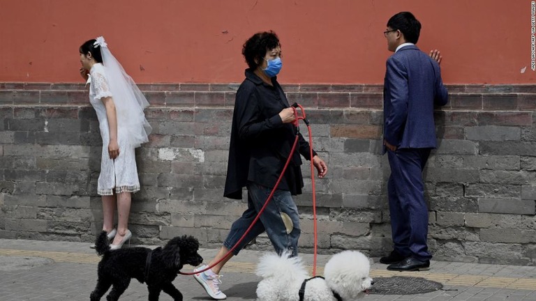 結婚写真を撮影中のカップルと、その前を飼い犬と通り過ぎる女性（北京＝５月１６日）/JADE GAO/AFP/AFP via Getty Images