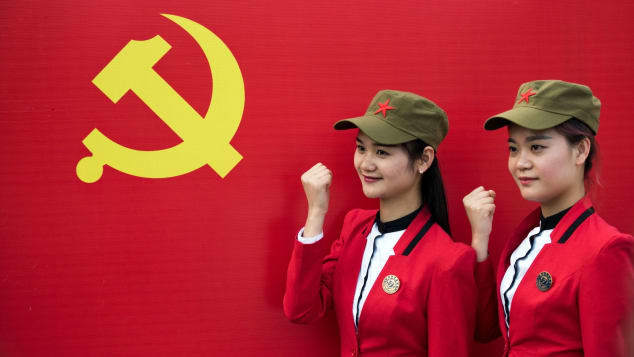 湖南省韶山郷でそろいの衣装に身を包み、共産党の旗の前でポーズを取る観光客（２０１６年撮影）/JOHANNES EISELE/AFP/Getty Images