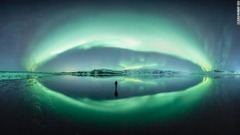 アイスランドのオーロラ。河口で冬の夜空が完全に反射されているのに遭遇した写真家が撮影。まずは風景を撮影し、その後氷の上に立つ自分の姿を納めた