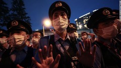 会場周辺で抗議運動する小規模な集団に手のひらを向ける警察官