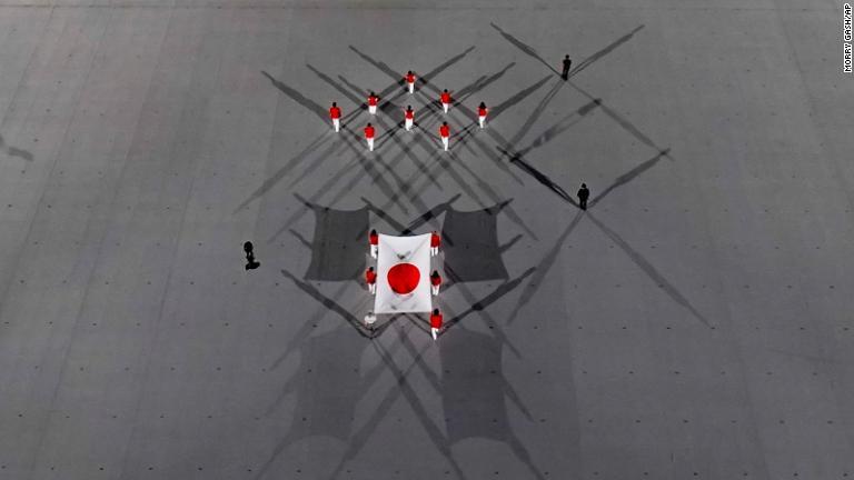 日本国旗が会場に運ばれる。国歌が歌われた後、新型コロナウイルス感染症で亡くなった世界中の犠牲者に黙とうをささげた/Morry Gash/AP
