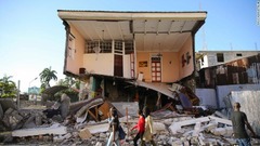 地震で壊れた家の前を歩く人々＝レカイ