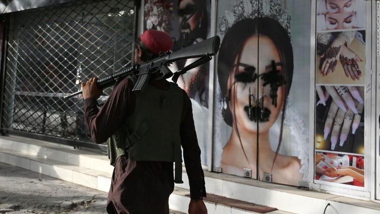 スプレーで汚された美容サロンの前を通るタリバーンの戦闘員＝１８日、アフガニスタン・カブール/WAKIL KOHSAR/AFP/AFP via Getty Images