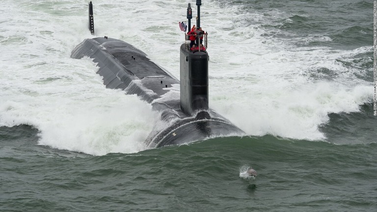 演習中の米海軍攻撃型潜水艦「ジョン・ウォーナー」。前方でイルカが跳ねている/U.S. Navy photo courtesy of Huntington Ingalls Industries by ChrisOxley/Released