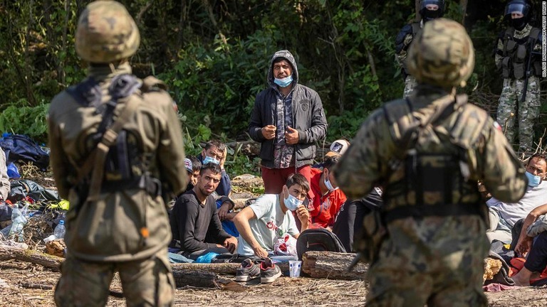 ポーランドとベラルーシの国境警備隊が国境付近のポーランドの村にいる移民のグループの側に立つ＝８月２０日/Wojtek Radwankski/AFP/Getty Images