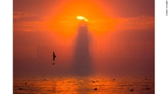 英イングランドにあるスカボロー埠頭灯台の写真。夕日に照らされ燃えているようだ