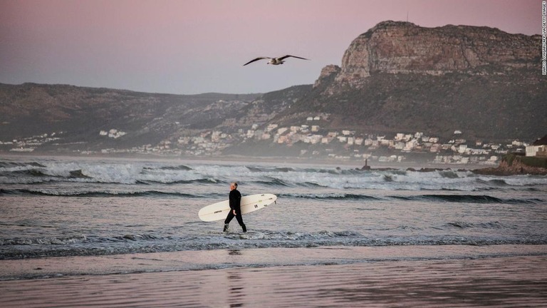 南ア・ケープタウンの浜辺でサーフィンをしようと海へ向かう人/MARCO LONGARI/AFP via Getty Images