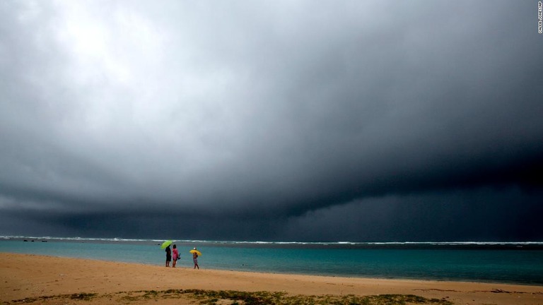 海岸で傘をさす人々＝６日、米ハワイ州ホノルル/Caleb Jones/AP