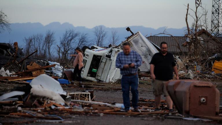 横転した車両やがれきのそばに立つ被災者＝メイフィールド/Brett Carlsen/Getty Images
