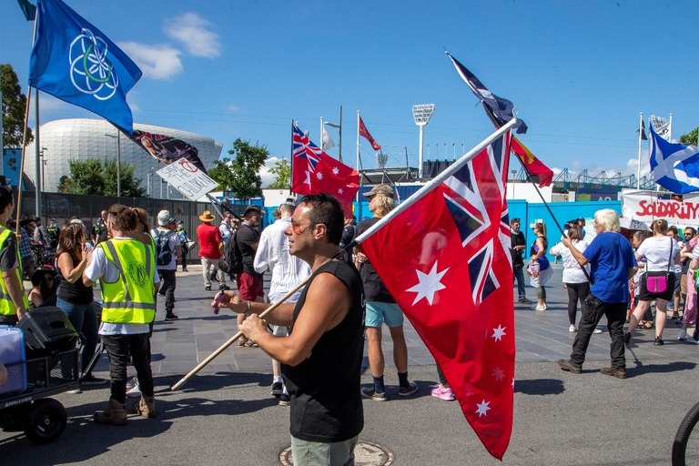メルボルンの競技場の外に集まり抗議する人々。赤色に変えた豪州国旗を手にする人も/Mark Baker/AP