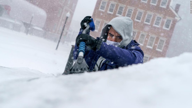 車のフロントガラスの雪かきをする男性＝２９日、ロードアイランド州プロビデンス/David Goldman/AP