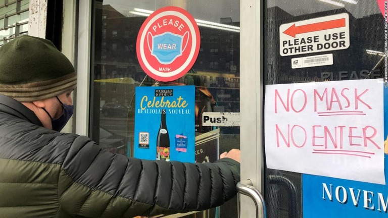 マスク非着用の入店禁止が書かれたドアを開ける男性＝米ニューヨーク/ Lindsey Nicholson/UCG/Universal Images Group/Getty Images