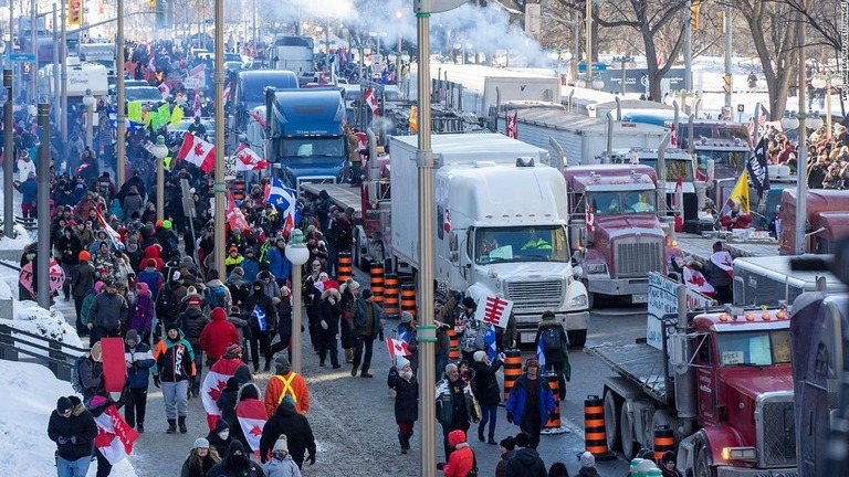 カナダ国旗を掲げ、コロナ規制に反対して議会周辺を練り歩く人々とトラックの車列/Lars Hagberg/AFP/Getty Images